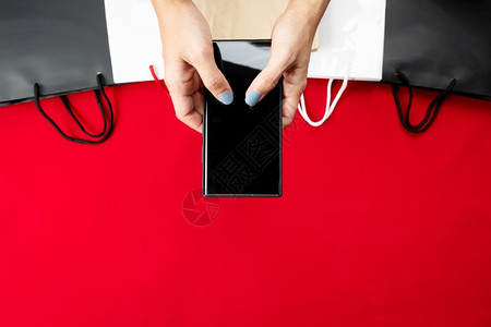 smartphone妇女手在智能机上用红背景的购物袋买下智能手机Smartphone红色的海报女士设计图片
