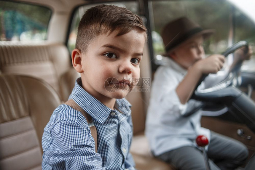 两个穿古老衣服的白人小男孩坐在一辆旧车里汽旅行轮图片