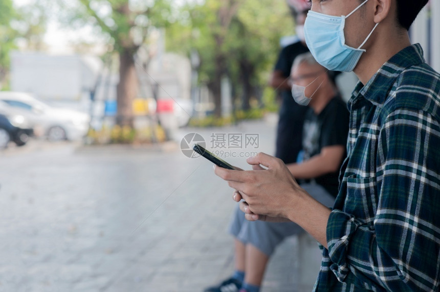 疾病预防亚洲男子手持移动电话坐着保持社会不动在共食19或Corona后新常态距离图片