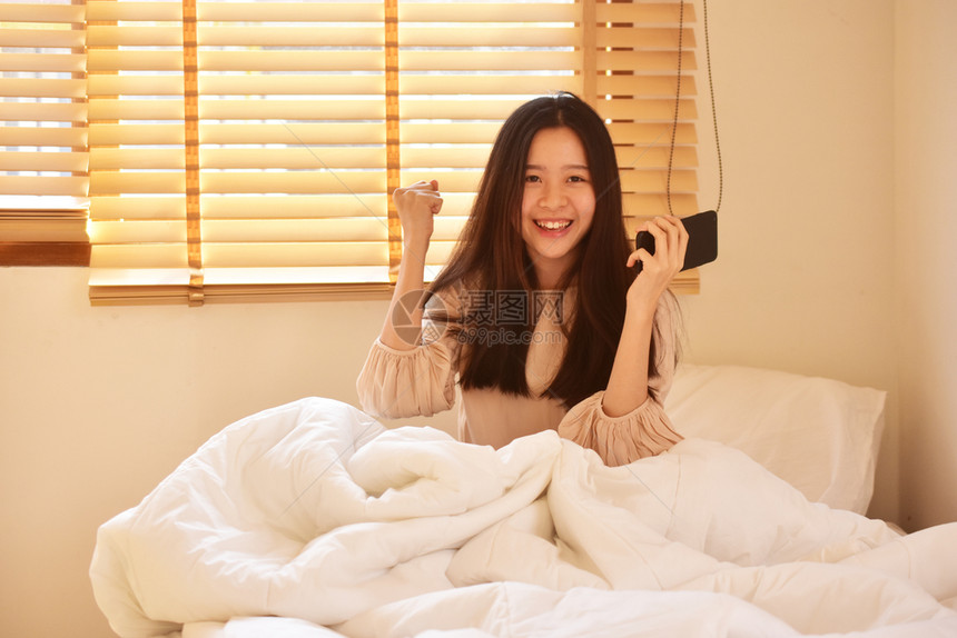 使用移动智能手机的妇女是离子卧室漂亮的家淑女图片