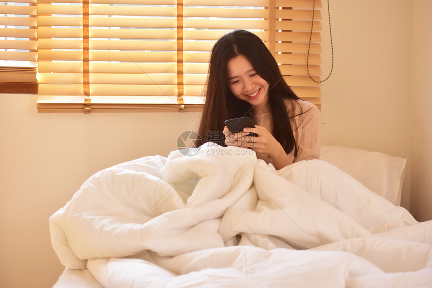 床使用移动智能手机的妇女是离子卧室房间白色的图片
