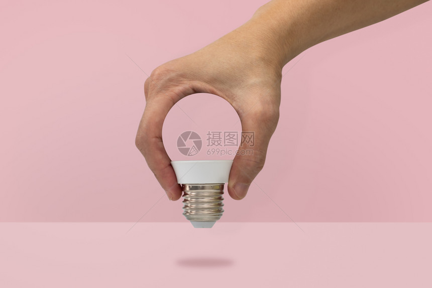 简单的明亮白色手握着在粉红背景上隔离的灯泡形状最小想法概念图片