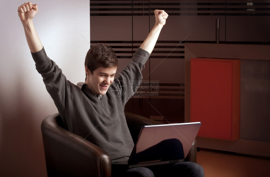 笔记本电脑室内的商人年轻举起手来争取胜利图片