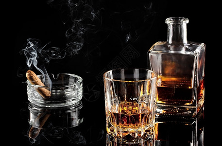 一杯加冰的威士忌和黑桌上蒸雪茄的一锅种玻璃食物图片