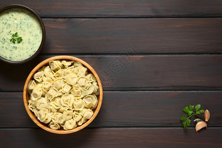 在木碗中煮熟的托尔特利尼配有奶油酱用自然光照在黑木头上饺子乡村脐图片
