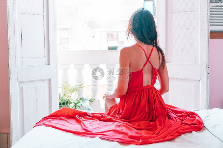 保持时尚女在古巴哈瓦那的旧公寓中穿着红色礼服的妇女在哈瓦那公寓的旧阳台上穿着红色礼服的年轻有吸引力妇女图片