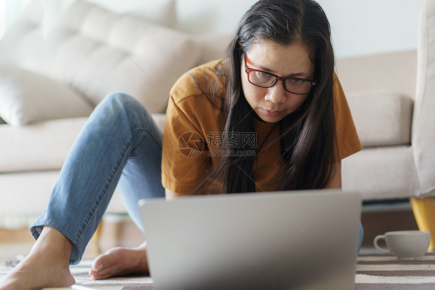 背部无线的学生女坐在地板上背着沙发坐在家中的客厅里她坐在家的起居室用沙发坐在地上图片