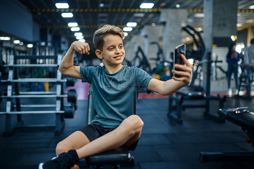 锻炼肌肉积极的有电话男孩在体育俱乐部保健和康生活方式的培训面青年运动员在体操板凳上做自拍有电话男孩在体操场上做自拍有电话男孩在体图片