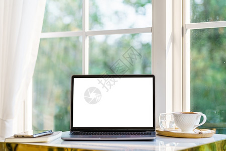 用笔记本咖啡杯和智能手机在白屏咖啡厅店窗户边的桌子上用空屏幕抽装手提电脑并填空白屏幕现代的自由职业者商图片