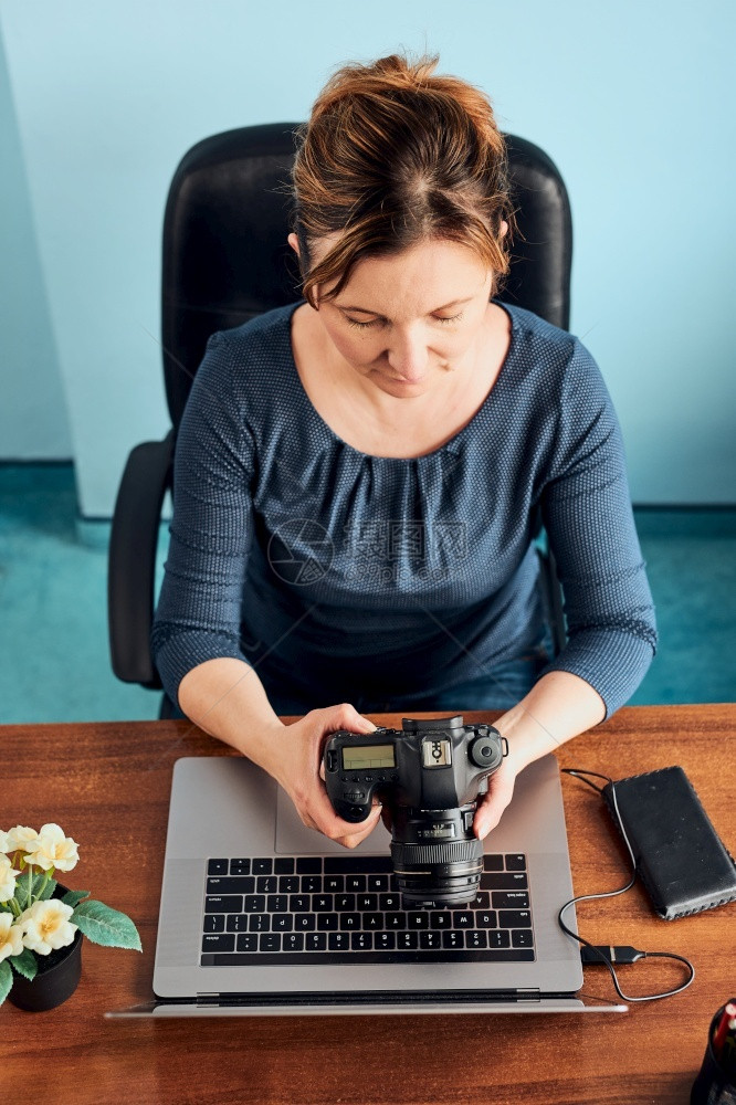 联系现代的在笔记本电脑和相机上拍摄照片的女影师妇编辑改用触摸浏览照片作为自由职业者坐在办公桌旁修饰图片