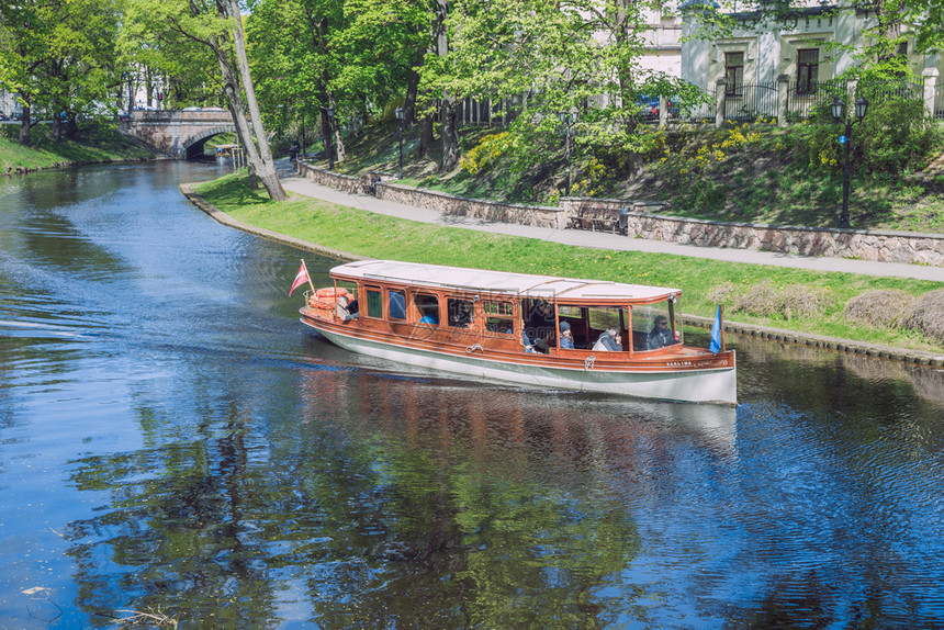 欧洲的2019年5月7日在拉脱维亚里加市旅游客乘船穿过城市运河环绕树木和自然绿色图片