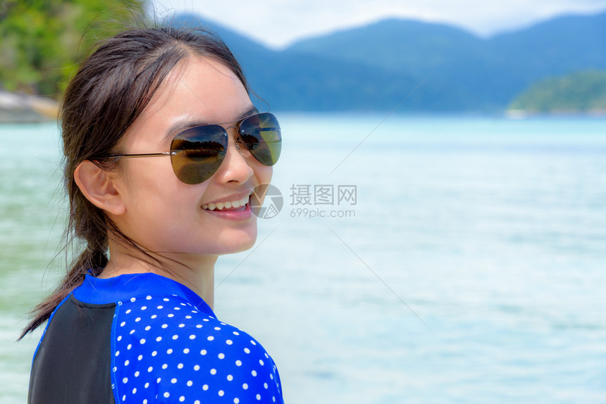 身戴太阳眼镜的女子脸在镜头前转动微笑着看摄影机在美丽的海洋自然景观和岛屿背上有一个快乐的节日一个女人脸朝海背景的相机微笑着海岸转图片
