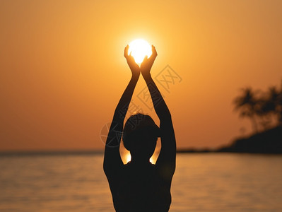假期黄色的太阳在橙天空的海面上女人站在海滩上阳光握在她的手中风景优美图片