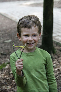 景观树戳带着临时弹弓的微笑男孩在夏季森林公园图片