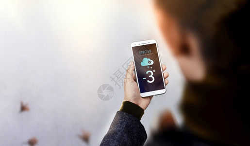 未来展示冬季年轻男子穿着暖身衣漫步使用手机在屏幕顶端查看天气预报时Snow是即将到来的感知寒冷天气雪背景图片