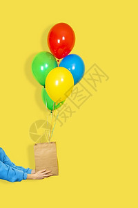 黄色的惊喜一种女手拿着纸袋和一束气球销售或呈现概念绿色红黄和蓝气球棕纸袋和手在黄背景上隔开女手拿着纸袋和一束气球绿色棕纸袋和黄背背景图片