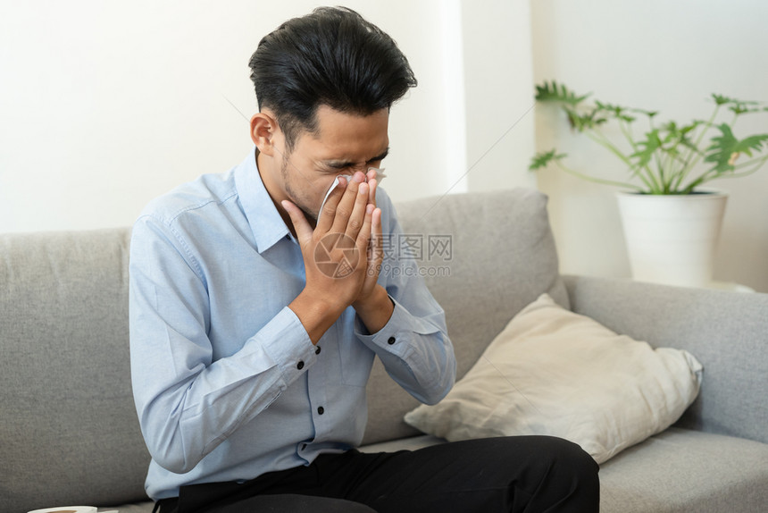 坐在沙发上感冒擦鼻涕的男性图片
