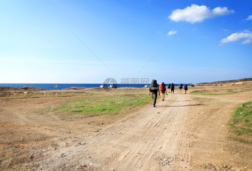 徒步旅行一群背包车在阳光灿烂的天空背景下沿海边一条沙路行走的背包车夏天自由图片