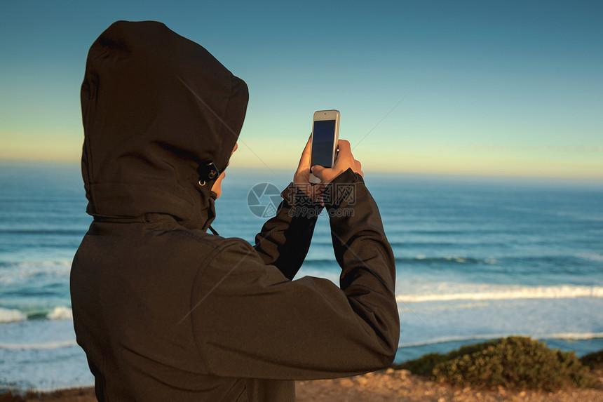 女士户外日出人用手机在海滩上拍照然后去海边图片