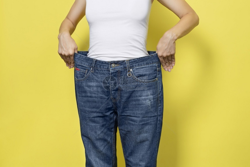 损失身体饮食适当营养减肥的概念穿着宽松牛仔裤的苗条女人和她减肥女人白色T恤和黄背景中突显的超大号牛仔裤饮食减肥的概念穿着宽松牛仔图片