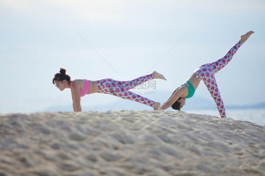 美丽的松弛两个女人在海边做瑜伽姿势快乐的图片