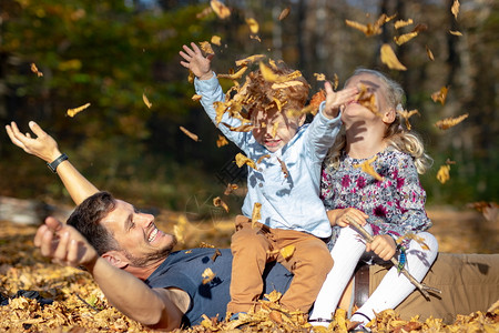 丰富多彩的扔投掷快乐爸和孩子们在森林里玩秋叶图片