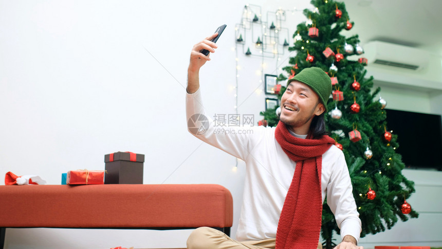 年轻的亚洲人带着自拍通过智能电话的视频呼叫坐在家中圣诞庆典派对上快乐地回家技术庭圣诞老人图片