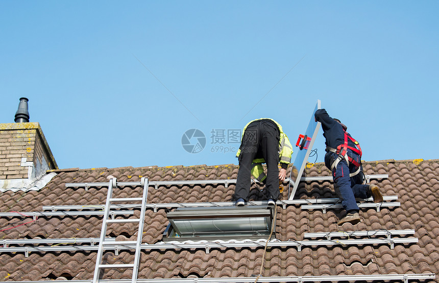 把太阳能电池板安装在屋顶上的工人图片