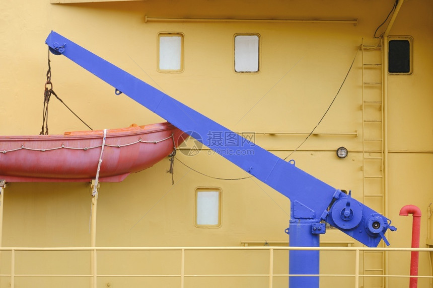 在货船一侧有小型蓝色起重机蓬隆的橙色救生艇前视角安全工程黄色的图片