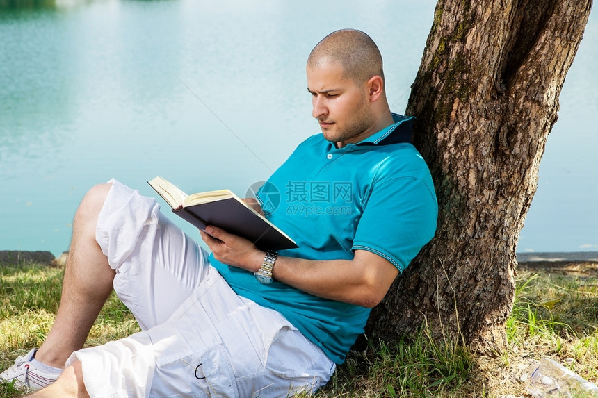 坐在大树旁边看书的年轻人图片
