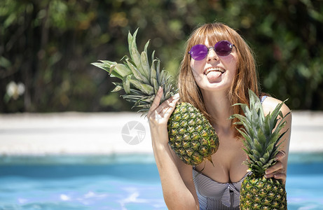 白种女孩带着太阳眼镜在游泳池里拿着两个菠萝唱歌水池情绪图片