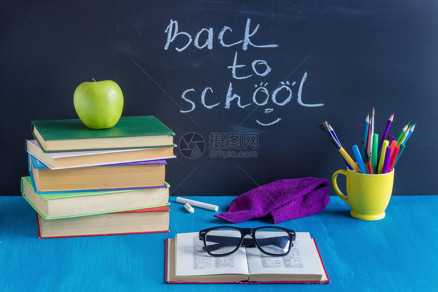 回到学校的概念教育科书工作场所学生书籍文具眼镜和绿色苹果蓝桌背景黑纸板文体眼镜绿苹果在布卢笔黄色的背部图片