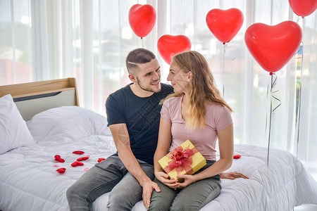已婚在情人节概念中爱情夫妇在卧室里赠送礼物盒的幸福浪漫床图片