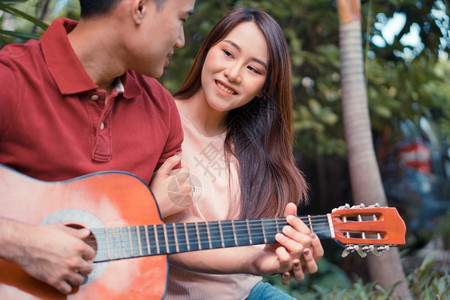 女朋友在花园里坐玩吉他和歌唱可记忆令人印象深刻的时概念情侣们乐趣快的图片