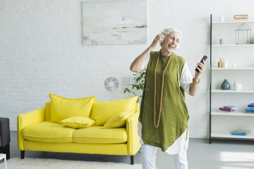手表墙微笑着的高级妇女通过手机听音乐耳技术图片