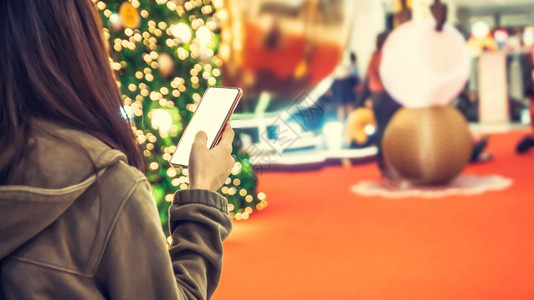 女士手持智能机的女人背景模糊圣诞节和树的火光照耀着圣诞树的火焰女电话图片