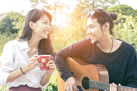 年轻的亚洲男女在公园里轻松地弹吉他女放松男人背景图片