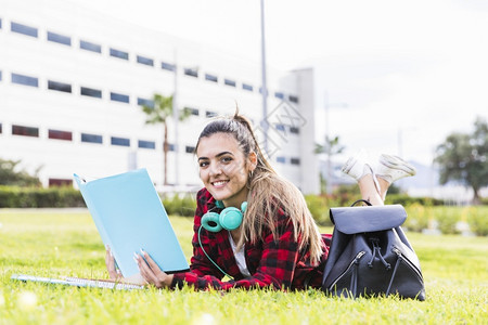 肖像笑着微的女大学生躺在绿色草地上拿着书手说谎喜悦图片
