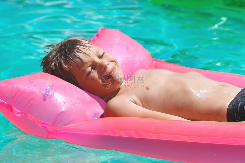 小男生微笑躺在游泳池的粉红色床垫上图片