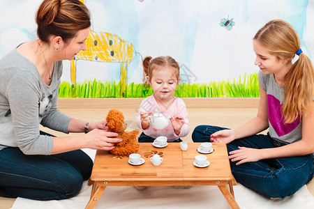 绘画小女孩在茶会上与母亲和姐一起玩耍使用儿童茶杯的会父母碗图片