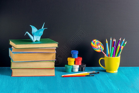 学生工作场所书籍文具油漆水粉和折纸鹤在蓝色桌子上的背景黑色板概念教育和回到学校生工作场所书籍文具油漆水粉和折纸起重机在蓝色桌子上背景图片