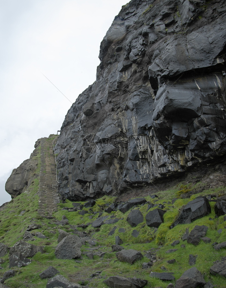 在法罗群岛瓦加尔的左侧用石头楼梯下雨后由火山起源的湿黑色岩壁垂直彩地形图像法罗群岛光荣景象法罗群岛的贺卡图案黑色明信片岩石图片