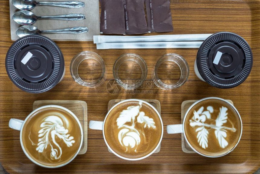 喝卷尾猴由拿铁艺术卡布奇诺玻璃水勺子糖和冰咖啡组成的套杯顶部景色木制板和餐桌饮料咖啡厅概念浓图片