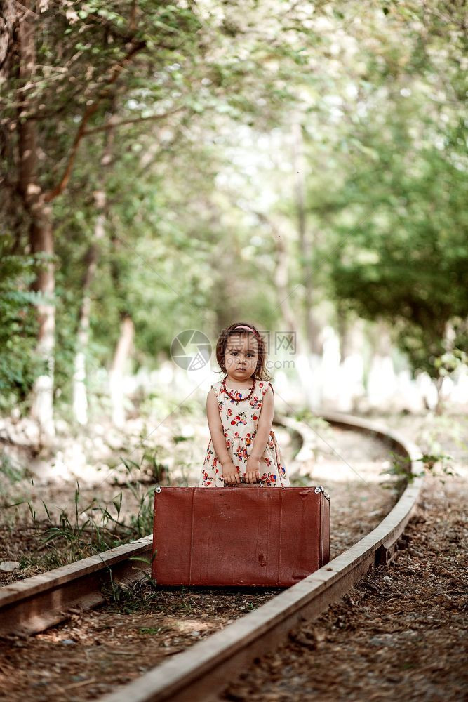 情绪化的穿着旧衣服可爱白种女孩在废弃铁路上装着旧式手提箱优质的图片
