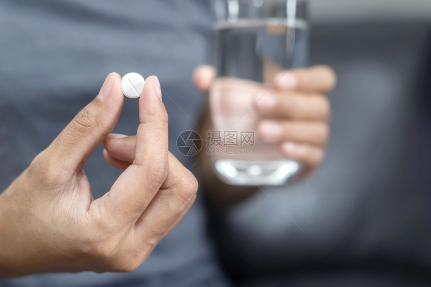 一名妇女拿着白药片和一杯水图片