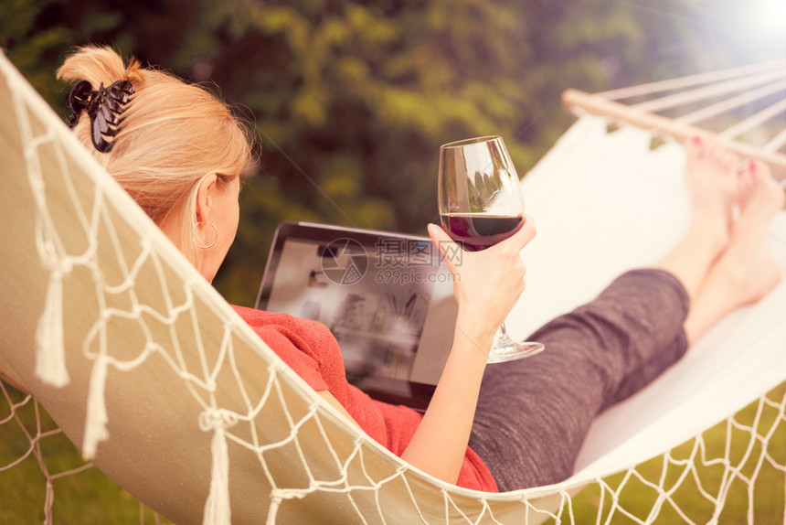 玻璃美丽的女人在吊床上放松用酒杯和浏览网络在平板电脑的古老效果上一种葡萄酒图片