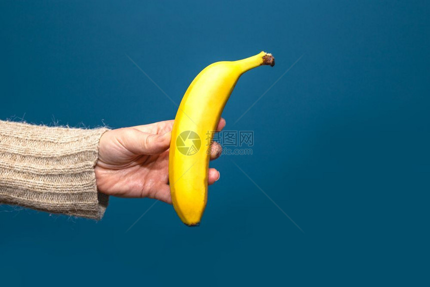 手持黄色香蕉果实的手在蓝色背景中分离手持黄色香蕉果实在蓝背景附近分离工作室可口甜的图片