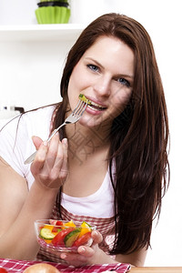 漂亮的年轻在厨房里吃沙拉的漂亮女人吃混杂沙拉的一顿饭图片