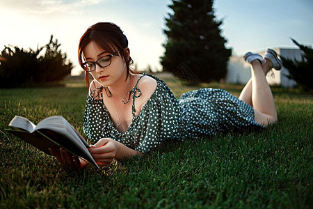 身着古老的代旧礼服天主教女孩在日落时读了一本关于草坪的书女士教育铺设图片