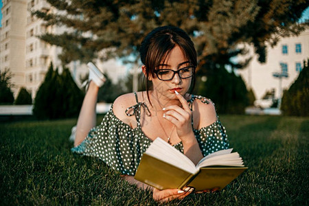 知识身着古老的代旧礼服天主教女孩在日落时读了一本关于草坪的书松弛坐着图片